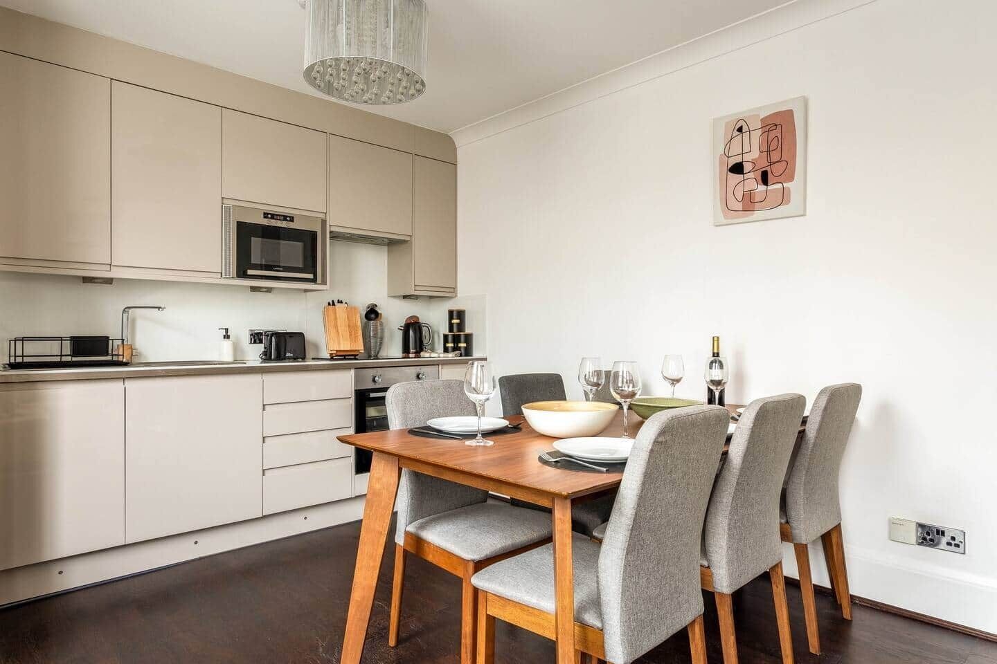 A modern kitchen with a dining area, featuring a wooden table and grey upholstered chairs.