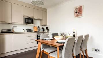A modern kitchen with a dining area, featuring a wooden table and grey upholstered chairs.