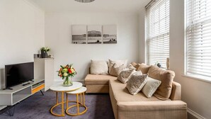 Ein modernes Wohnzimmer mit einer Couch, einem Fernseher und einem runden Tisch mit einem Blumenstrauß.