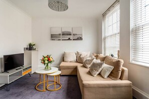 A modern living room with a sofa, TV, and a round table with a vase of flowers. - 20 West Street BN1 2RS (Brighton and Hove)