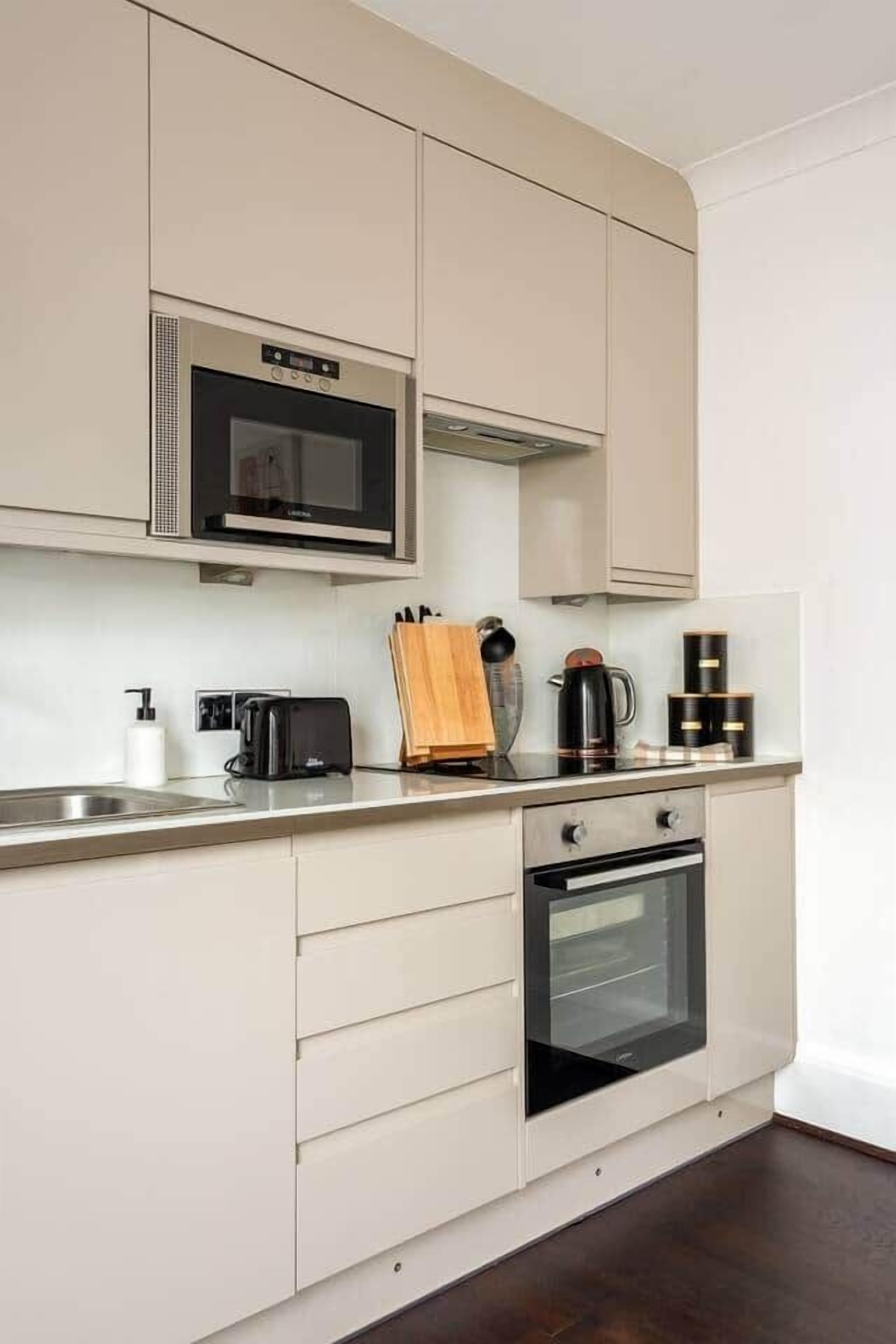 A modern kitchen with white cabinetry, a built-in microwave, a toaster, a coffee maker, and a stove.