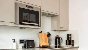A modern kitchen with white cabinetry, a built-in microwave, a toaster, a coffee maker, and a stove.