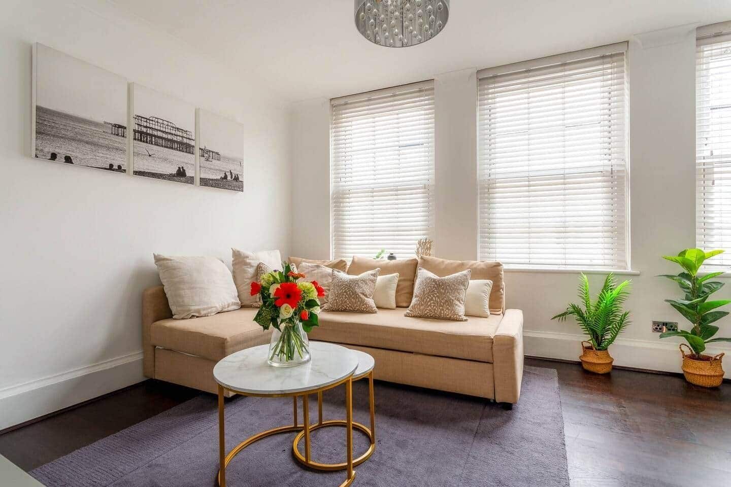 A living room with a beige sofa, a round coffee table, and two windows with blinds.