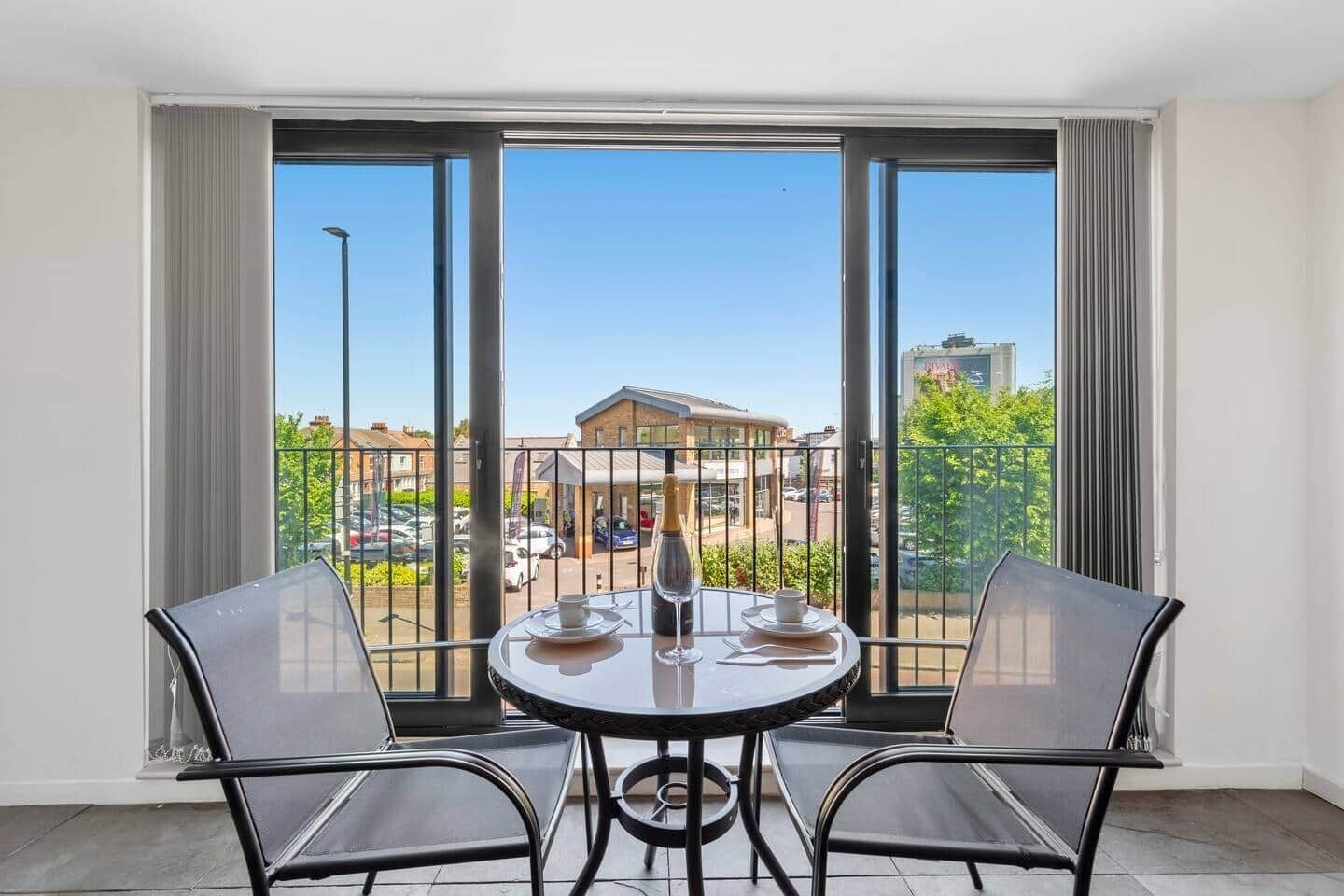Ein Balkon mit Tisch und Stühlen, einer Champagnerflasche und Blick auf ein Gebäude sowie geparkte Autos.