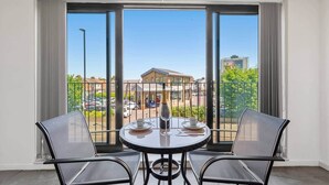 En balkon med et bord og stole, en champagneflaske og udsigt til en bygning samt parkerede biler.