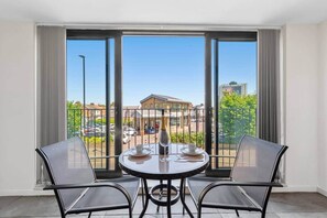 A balcony with a table and chairs, a bottle of champagne, and a view of a building and parked cars. - Flat 2, Brentford TW8 9NA (Brentford)