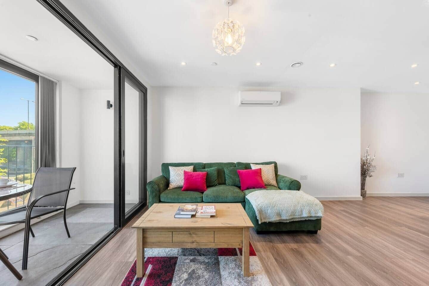 A modern living room with a green sofa, a wooden coffee table, and a large window.