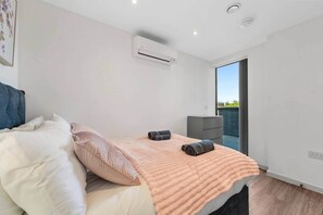 Un dormitorio con cama, almohadas, manta, unidad de aire acondicionado, un escritorio pequeño y vistas al exterior.