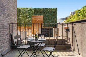 Una terraza en la azotea con una mesa, sillas, una botella y un vaso.