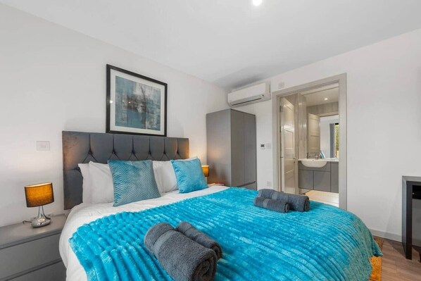 Una habitación de hotel con cama, lámpara de noche, un cuadro en la pared y un baño visible a través de una puerta abierta.