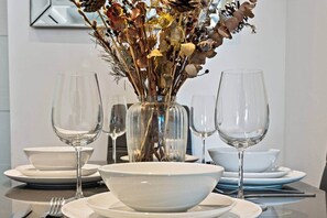 A dining table set with white plates, bowls, and clear wine glasses, centered around a vase with dried flowers and foliage. - Flat 2, Brentford TW8 9NA (Brentford)