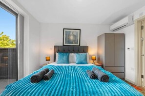 Habitación de hotel con una cama grande, dos lámparas de noche, un cuadro enmarcado sobre la cama y un equipo de aire acondicionado en la pared.
