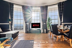 Un salon moderne doté d’une grande fenêtre, d’un téléviseur à écran plat, d’un coin repas et offrant une vue sur la mer.