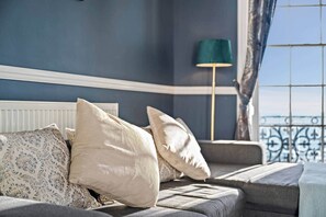 Ein Zimmer mit einem Bett, einem Sessel und Blick durch ein Fenster mit Metallgeländer.