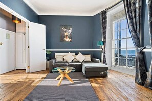 A living room with a sofa, a coffee table, and a view of the sea through a window. - 68 Marine Parade - BN2 1AD (Brighton and Hove)