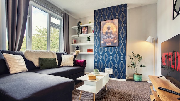 Uma sala de estar moderna com um sofá, uma mesa de centro, estante, parede decorativa e uma televisão.