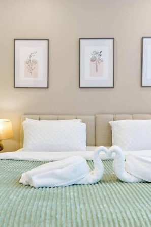 Ein Hotelzimmer mit einem Bett, zwei gerahmten Blumenbildern an der Wand und einem Paar Handtüchern, die auf dem Bett drapiert sind.