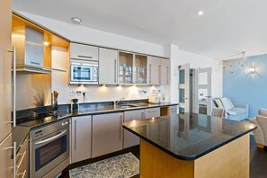 A modern kitchen with built-in appliances, a central island, and a seating area with a sofa and armchairs. - Princes House BN1 1EA (Brighton and Hove)