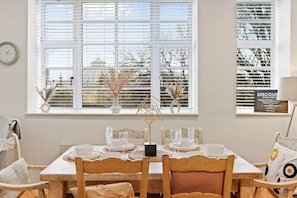 A dining area with a table set for four, white chairs, and a window with blinds. - Princes House BN1 1EA (Brighton and Hove)