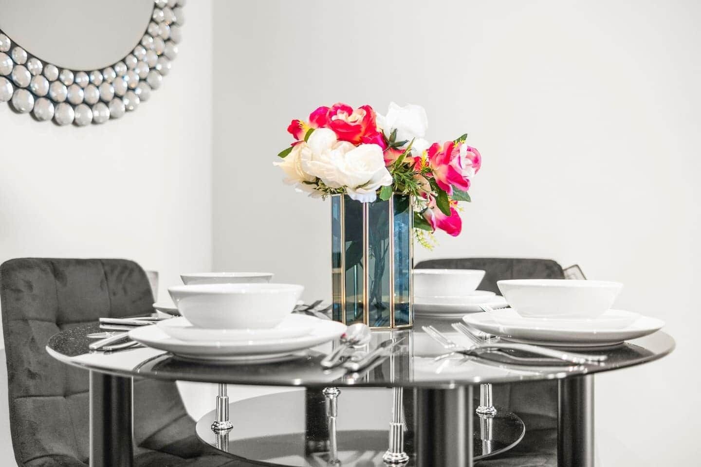 Una mesa de comedor con un florero, platos blancos y cubiertos.