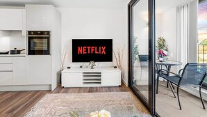A modern living room with a flat-screen TV mounted on a white console, a kitchen area with a built-in oven, and a dining area with a table and chairs. - Flat 5, Brentford TW8 9NA (Brentford)