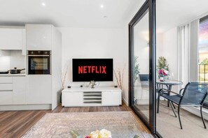 A modern living room with a flat-screen TV mounted on a white console, a kitchen area with a built-in oven, and a dining area with a table and chairs. - Flat 5, Brentford TW8 9NA (Brentford)