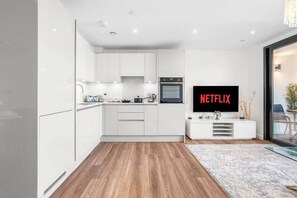 A modern kitchen with white cabinetry, a built-in oven, and a flat-screen TV displaying the Netflix logo. - Flat 5, Brentford TW8 9NA (Brentford)