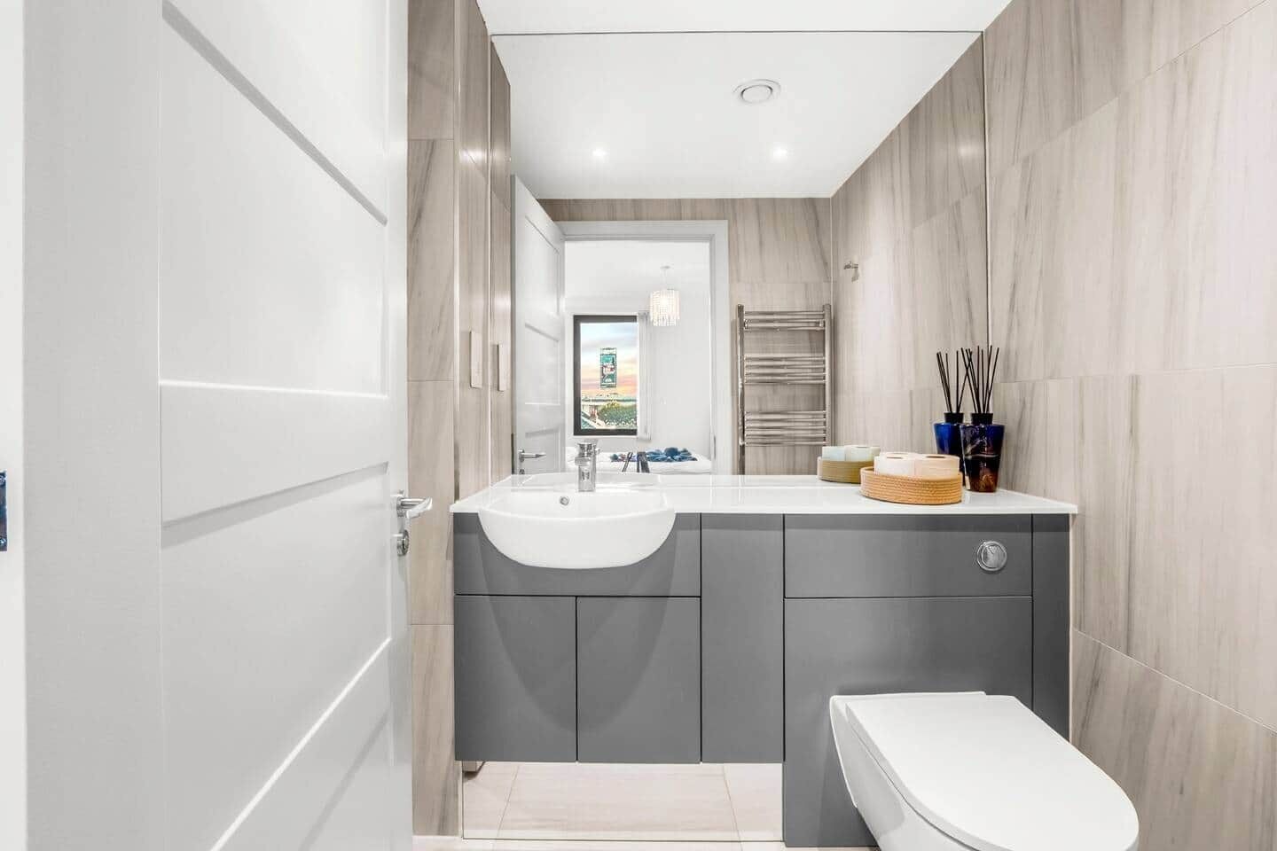 A modern bathroom with a white sink, grey cabinets, and a toilet.