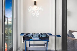 A room with a foosball table, a sofa, and a wall with a neon sign. - Flat 5, Brentford TW8 9NA (Brentford)