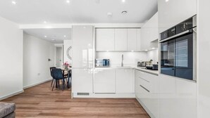 A modern kitchen with white cabinetry, a built-in oven, and a dining area with a black chair and a small table. - Flat 5, Brentford TW8 9NA (Brentford)