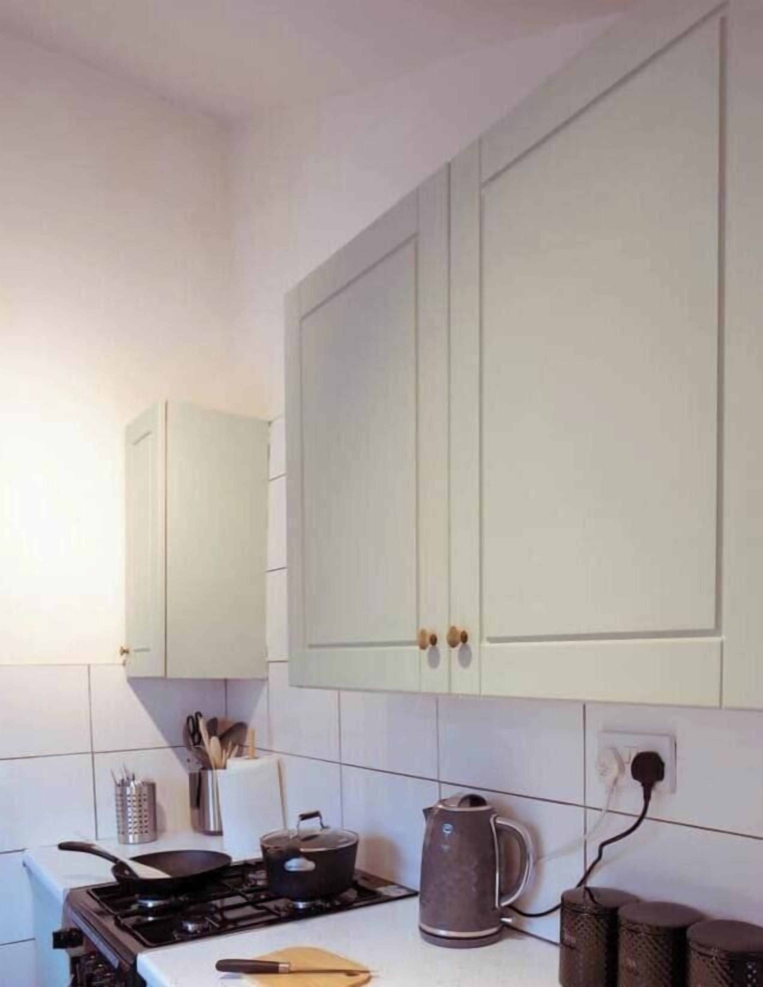A kitchen with a stove, a kettle, and cabinets.