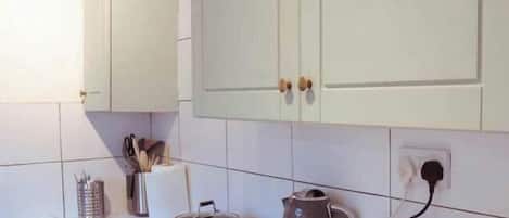 Una cocina con estufa, tetera y alacenas.