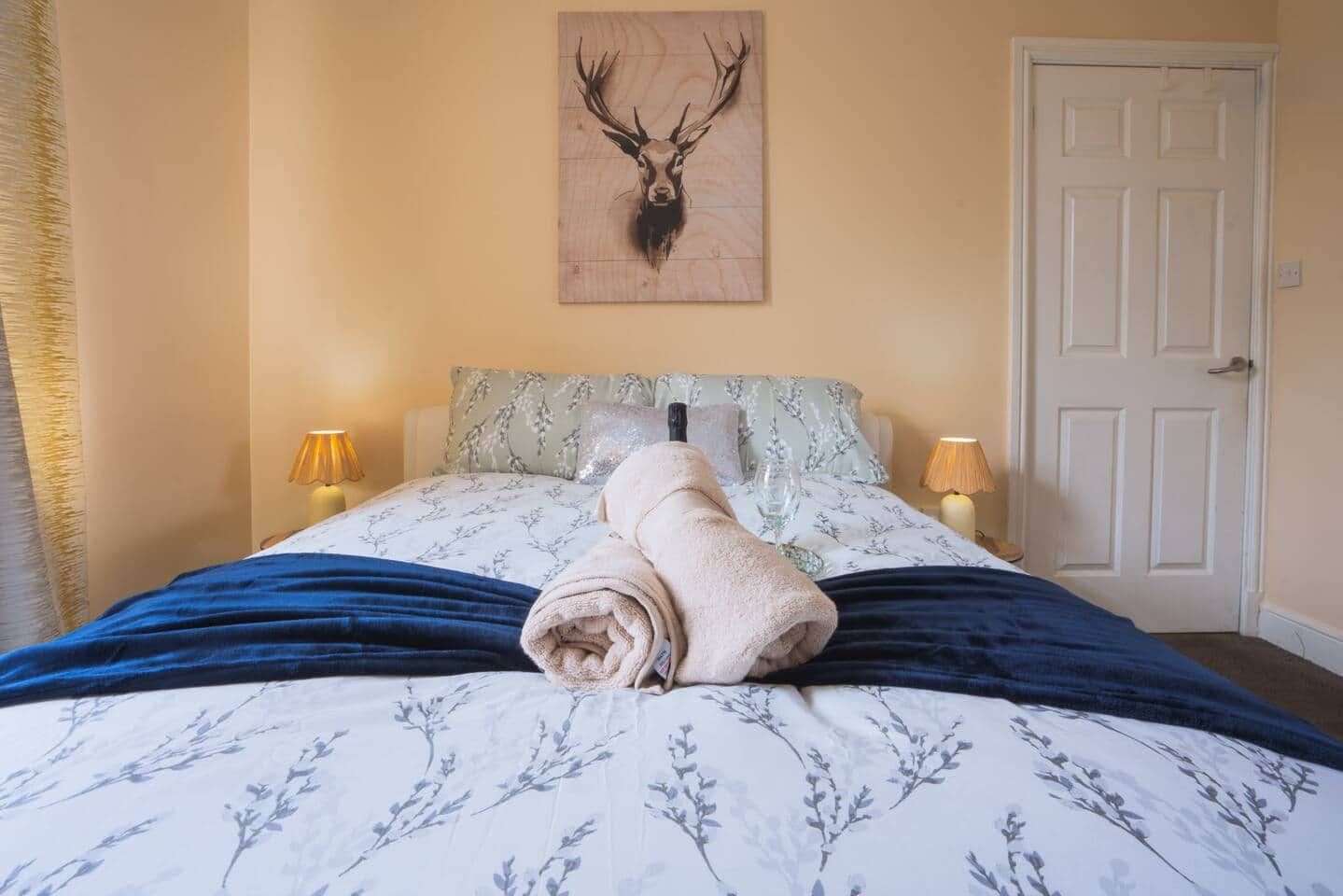 A bedroom with a bed, a wall-mounted deer head artwork, two bedside lamps, and a door.