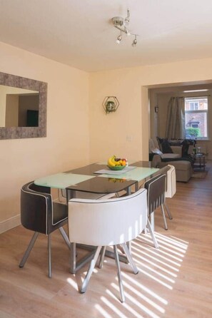 A dining area with a glass-top table, white chairs, and a fruit bowl. There is a mirror on the wall and a ceiling light fixture. - Fenham, Newcastle NE4 (Newcastle upon Tyne)