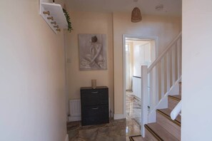 A hallway with a marble floor, a black cabinet, a painting on the wall, and a staircase leading to another room. - Fenham, Newcastle NE4 (Newcastle upon Tyne)