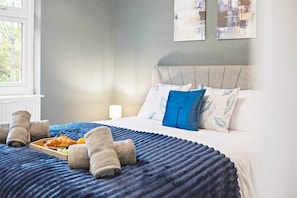 Quarto de hotel com cama, almofadas, um suporte com croissants e toalhas.