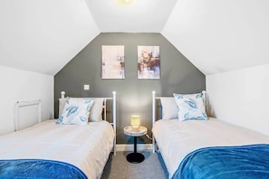 A bedroom with two single beds, a small bedside table with a lamp, and two wall-mounted paintings. - 18 Carrick Gardens, N17 7AX (London)