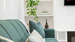 A living room with a green sofa, a white fireplace, and a wall-mounted TV displaying 'NETFLIX'. - 18 Carrick Gardens, N17 7AX (London)
