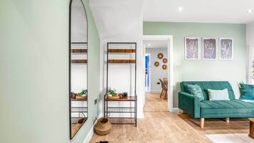 A modern living room with a green sofa, a large mirror, and a wooden floor.