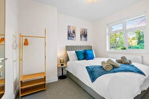 Ein Schlafzimmer mit einem Bett, einem Nachttisch, einer Lampe, einem Fenster mit Blick und einem Holzboden.