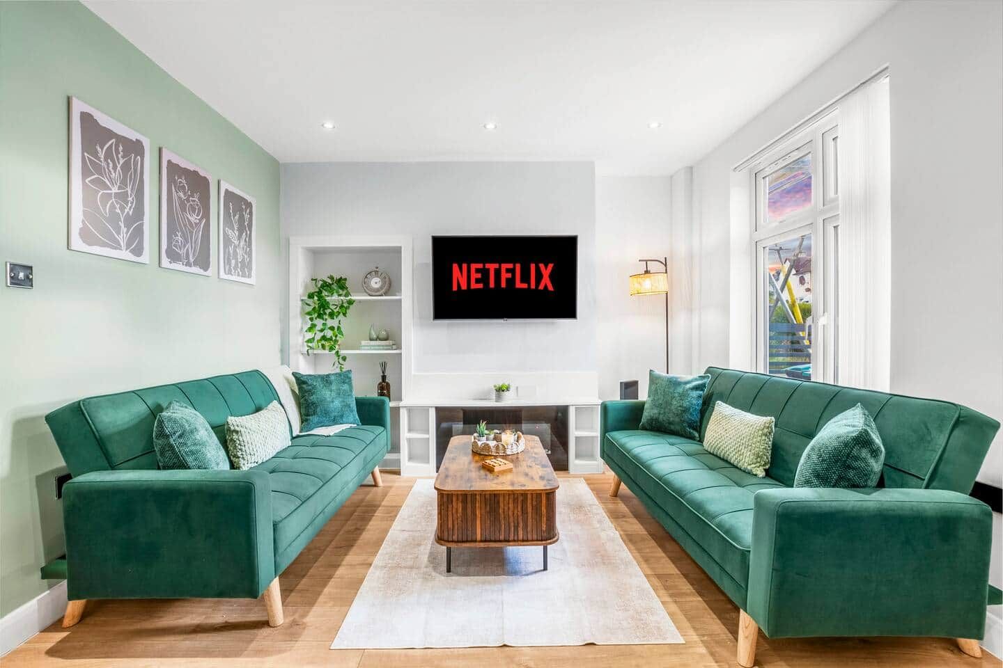 A living room with two green sofas, a coffee table, a flat-screen TV, and artwork on the walls.