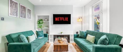 A living room with two green sofas, a coffee table, a flat-screen TV, and artwork on the walls.