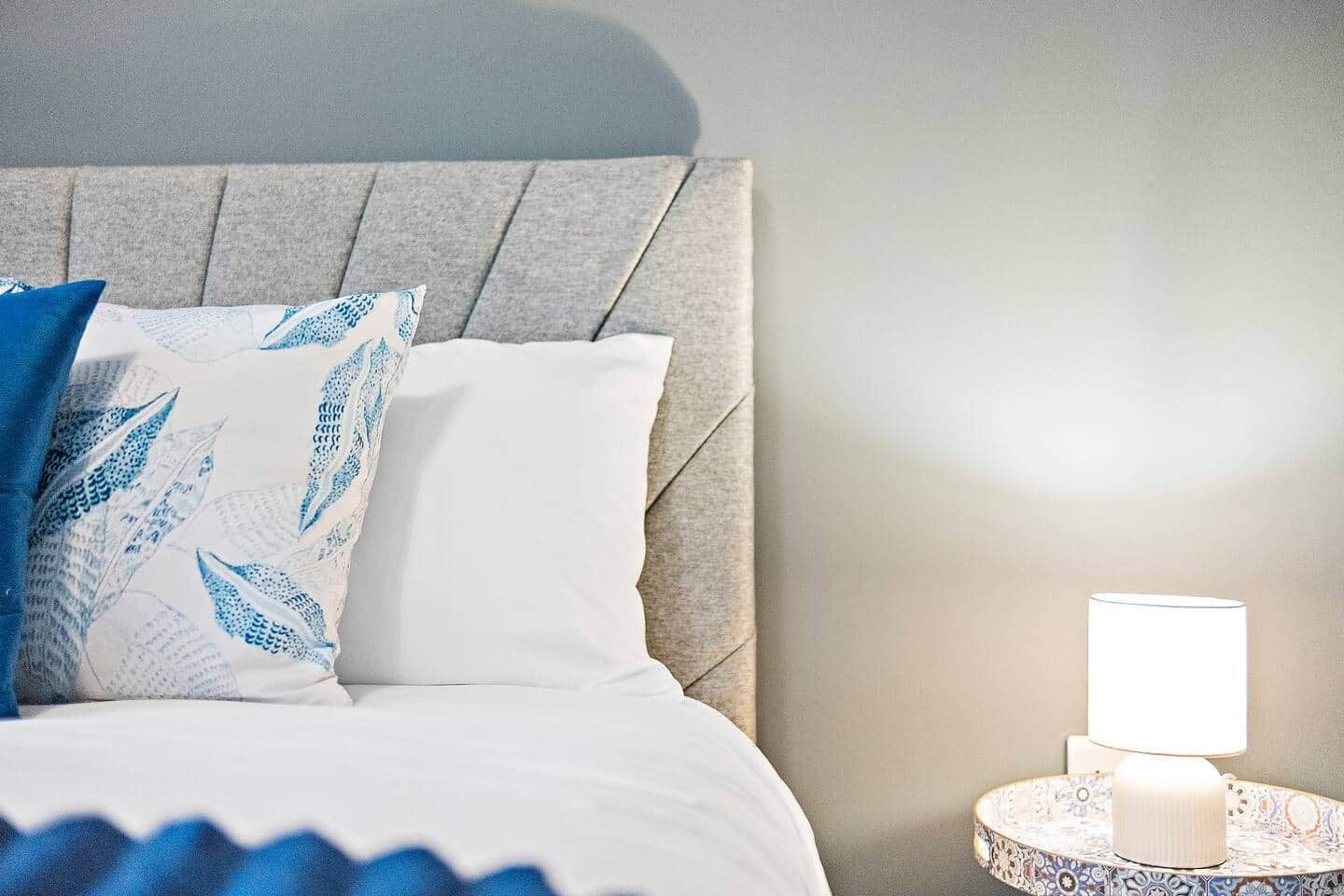 A neatly made bed with a headboard, a bedside lamp, and a decorative plate.