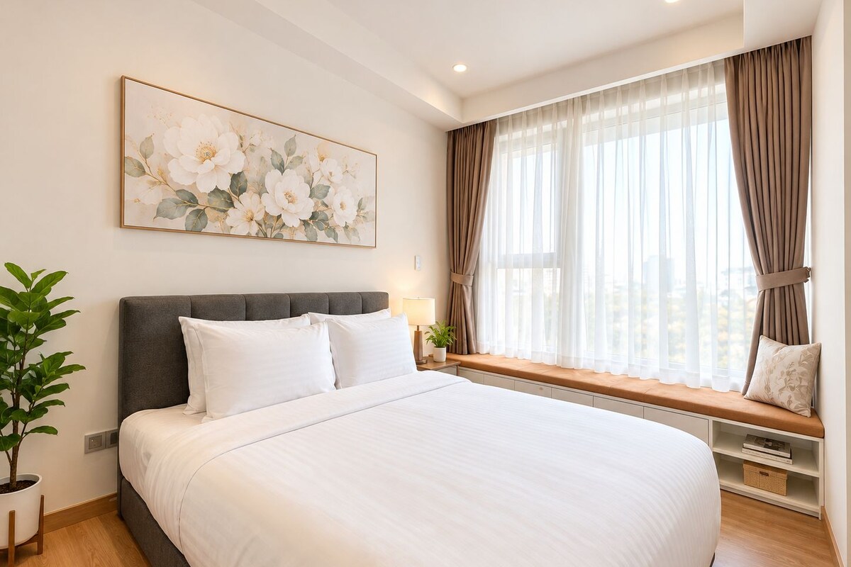 Una habitación de hotel con una cama grande, una ventana con cortinas, una mesita de noche con lámpara y un cuadro colgado en la pared.