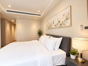 A hotel room with a bed, bedside table, lamp, and a wall-mounted air conditioning unit. - Midtown Rescidences Corporate (Ho Chi Minh City)