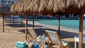 Ein Strand mit Strohdächern, Liegestühlen und einem Poolbereich mit Handtüchern und einem Tisch.