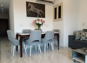 A modern dining area with a table and chairs, a vase of flowers, and a painting on the wall. - Hurghada stylish Apartment on the beach 204 (محافظة البحر الأحمر)