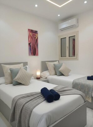 A hotel room with two beds, a painting on the wall, an air conditioning unit, and a bedside lamp. - Hurghada stylish Apartment on the beach 204 (محافظة البحر الأحمر)