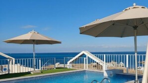 Ein Poolbereich mit Liegestühlen und Sonnenschirmen, ein klarer Himmel und Blick auf den Ozean.