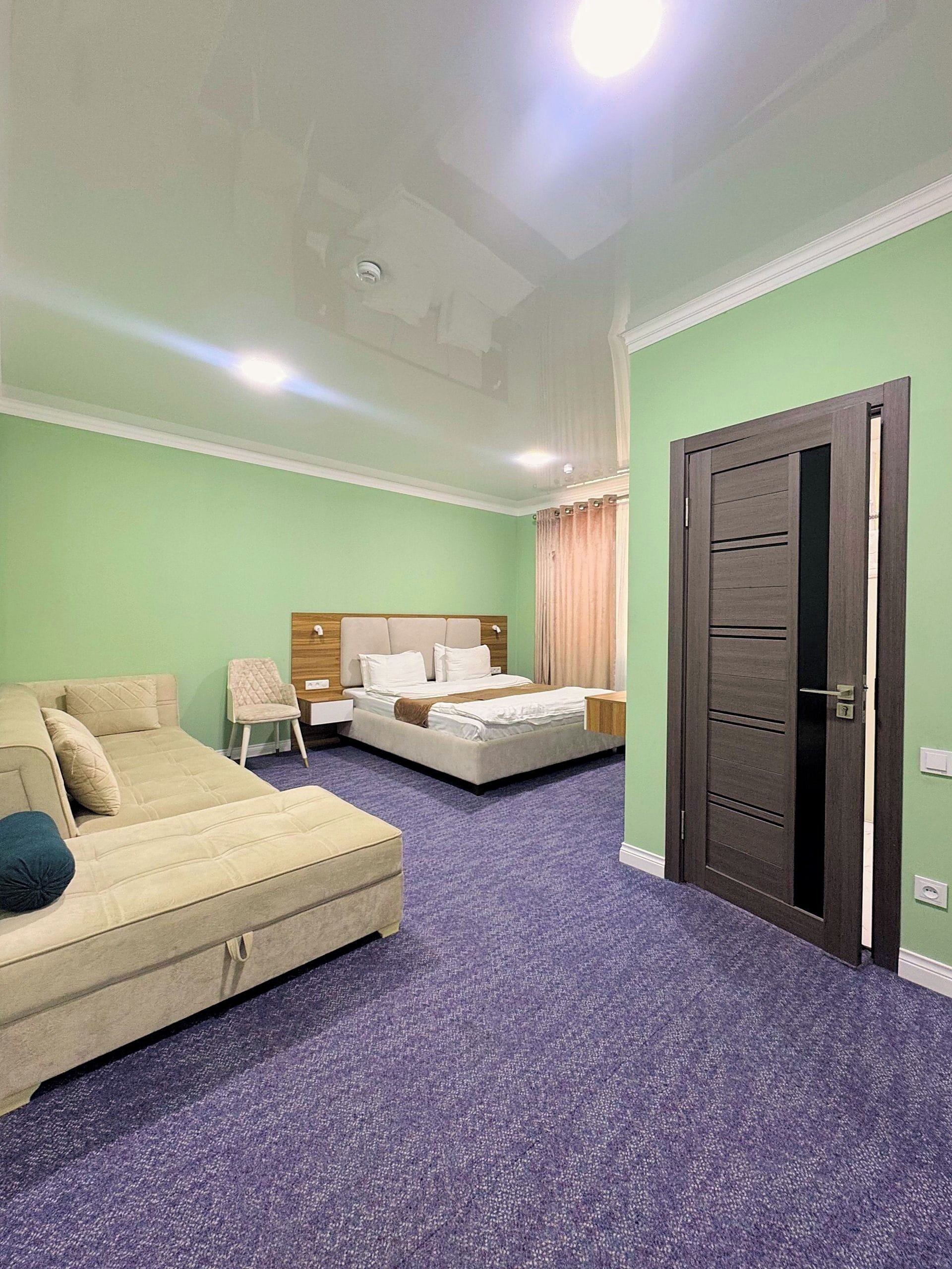 A hotel room with a bed, a sofa, a chair, and a door.
